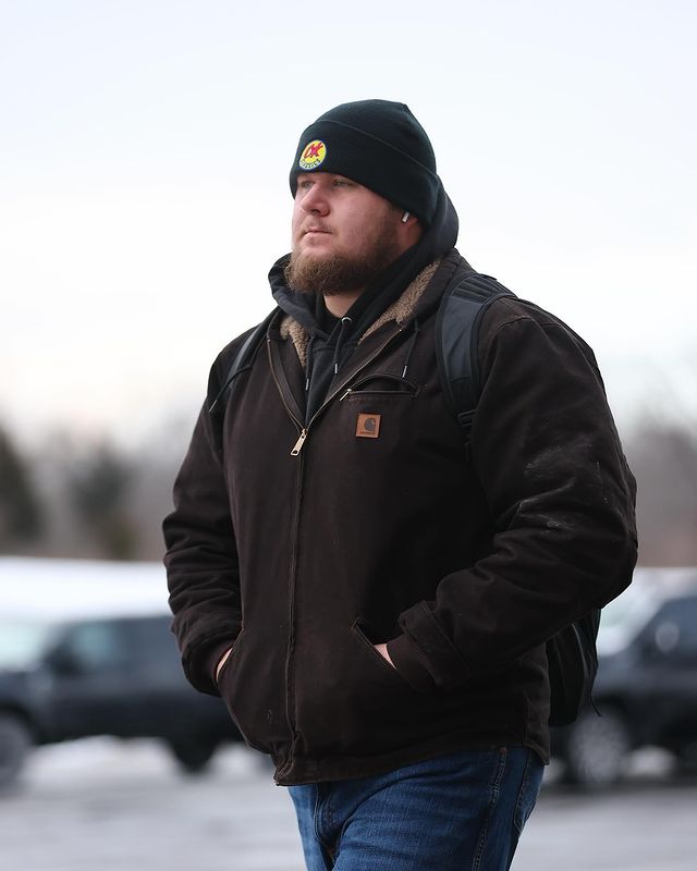 Humphrey wearing a hat and jacket walking in a parking lot